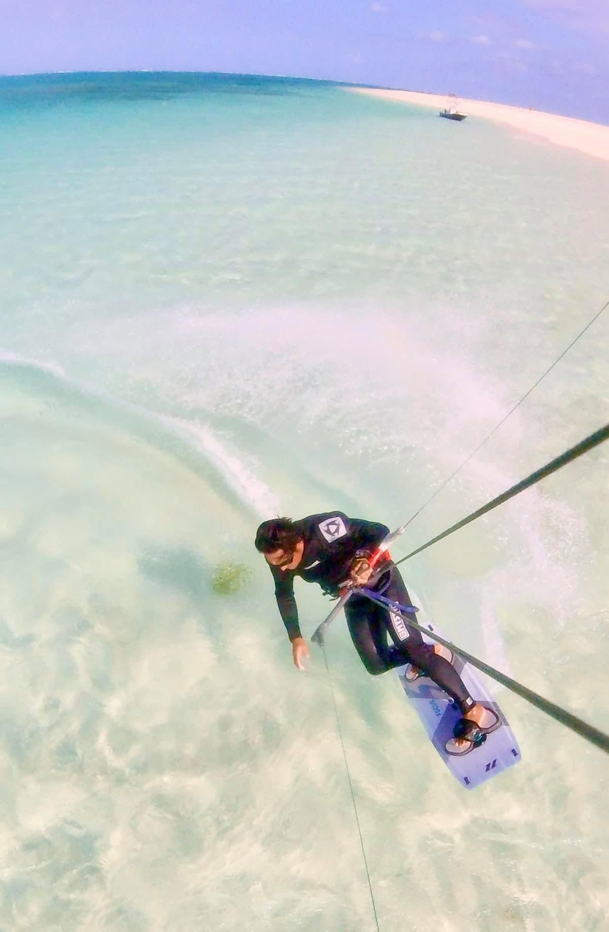Kitesurfer riding through shallow white-sand water, seen from above