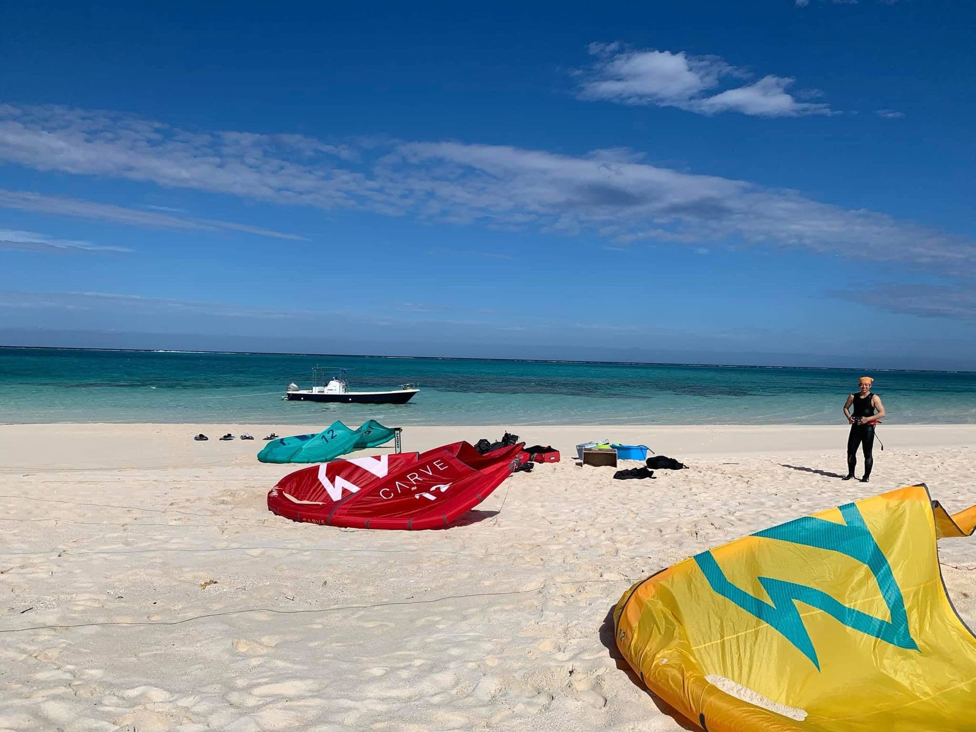 Kites and boards laid out on a white sand beach with a boat offshore