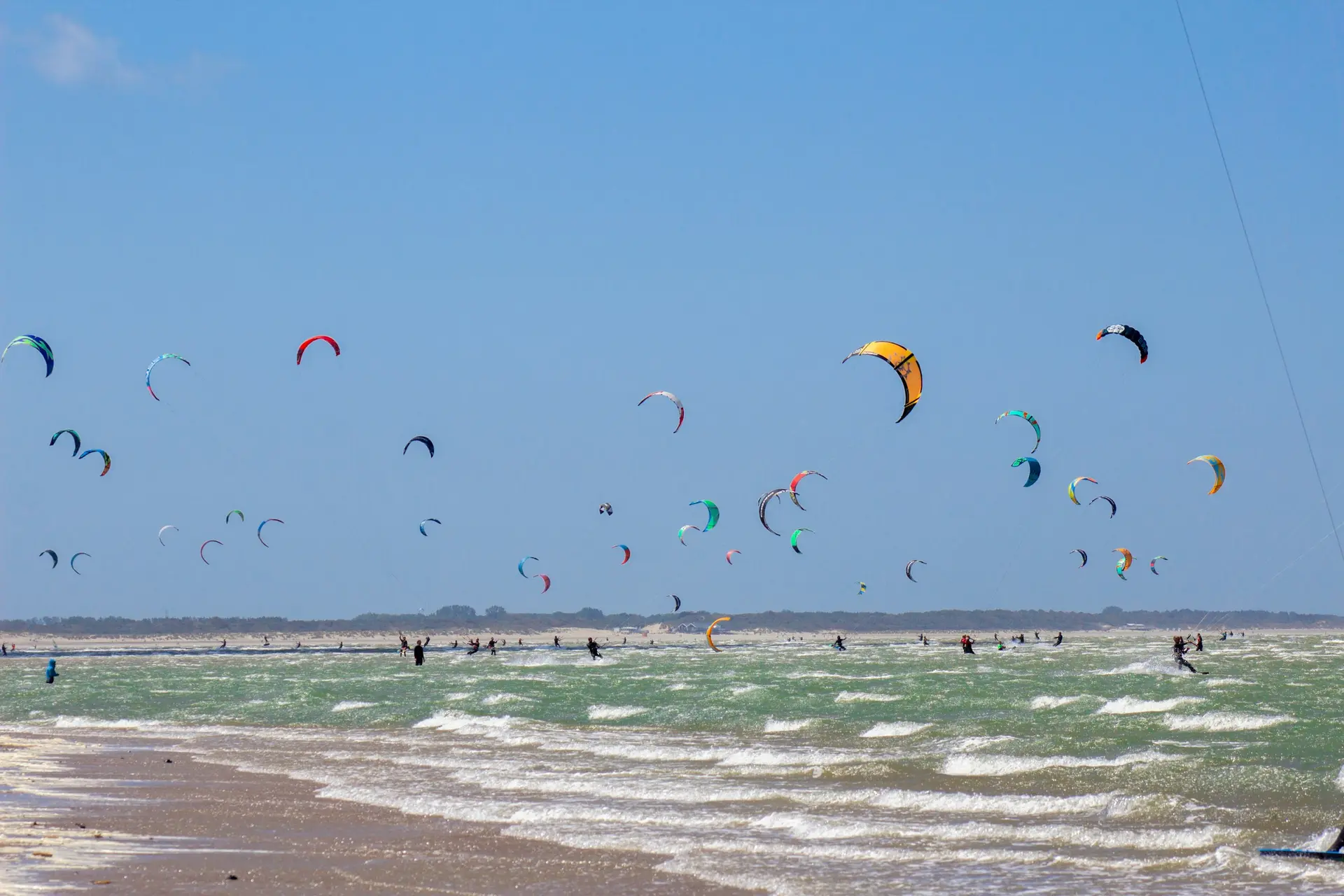 Dozens of kites over a beach and shallow, choppy water