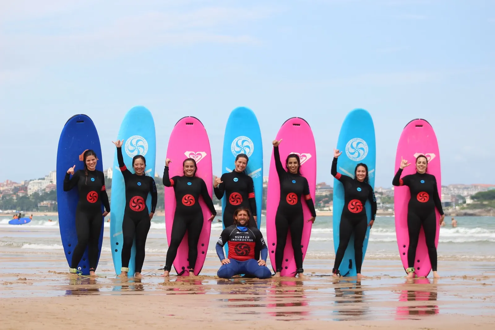 A surf class lined up with their boards on the sand at Somo, the instructor kneeling in front