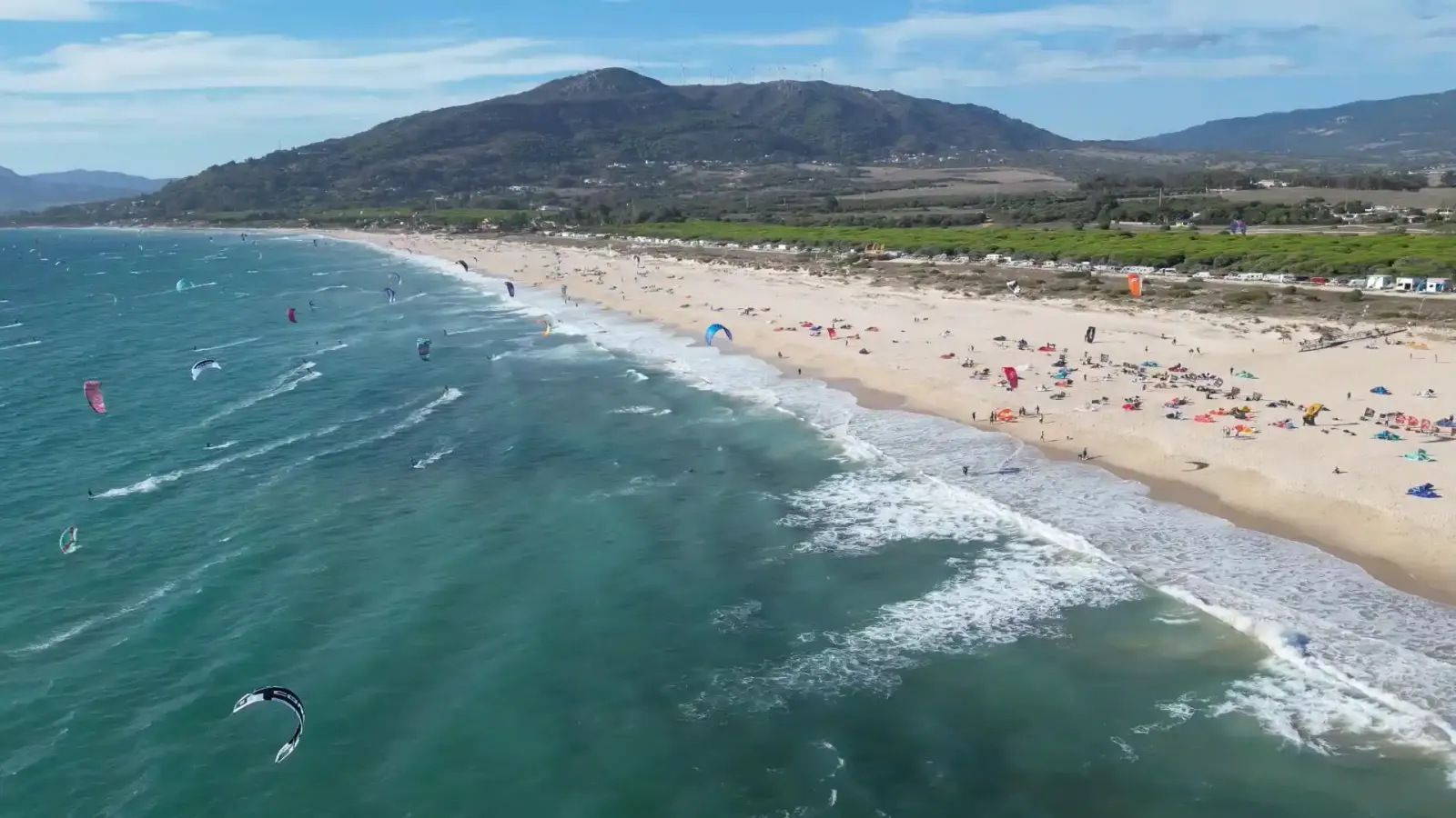 Aerial view of a long Tarifa beach with kites on the water and hills behind
