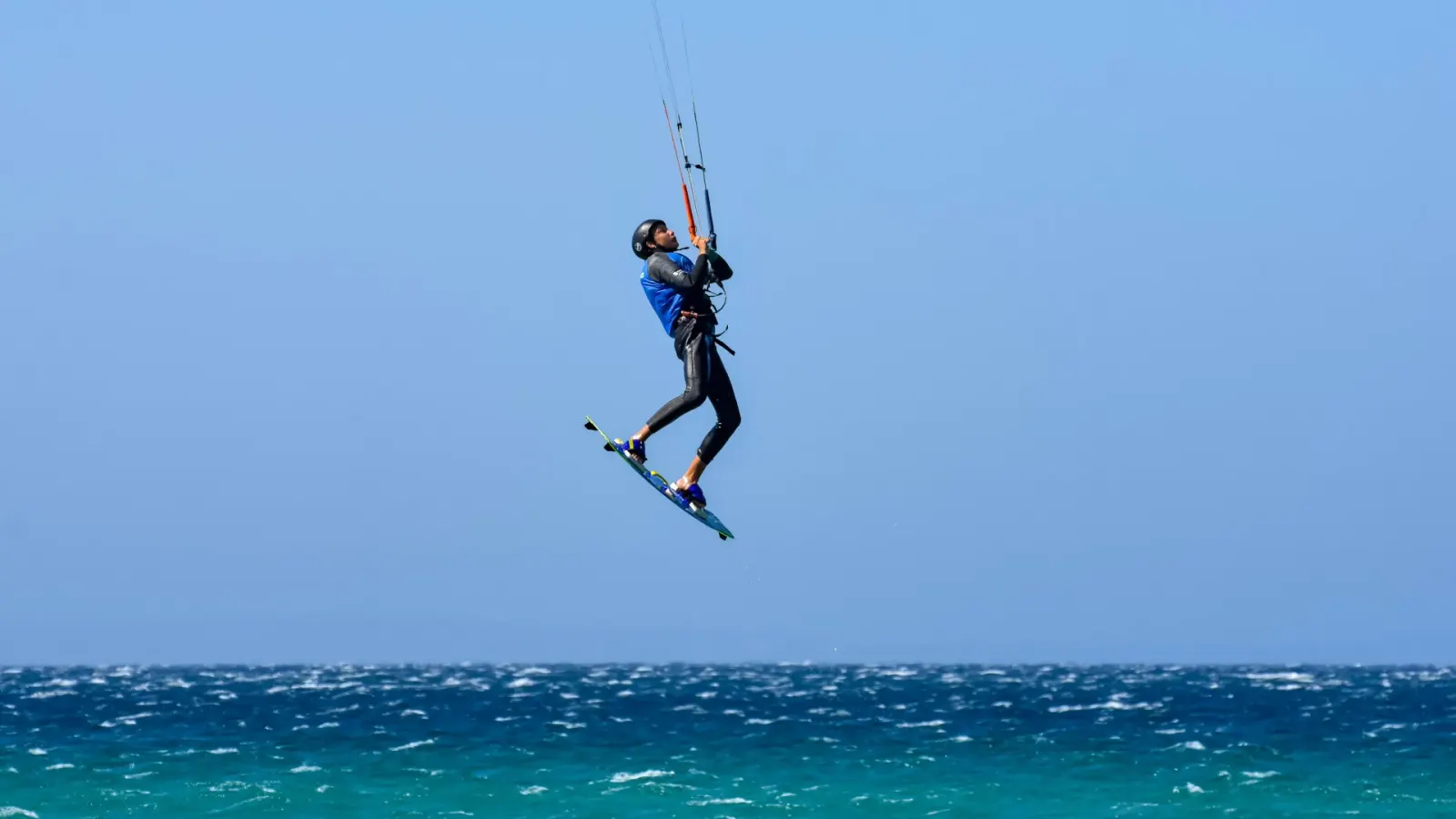 A kitesurfer in a blue lycra jumping high above choppy Levante water