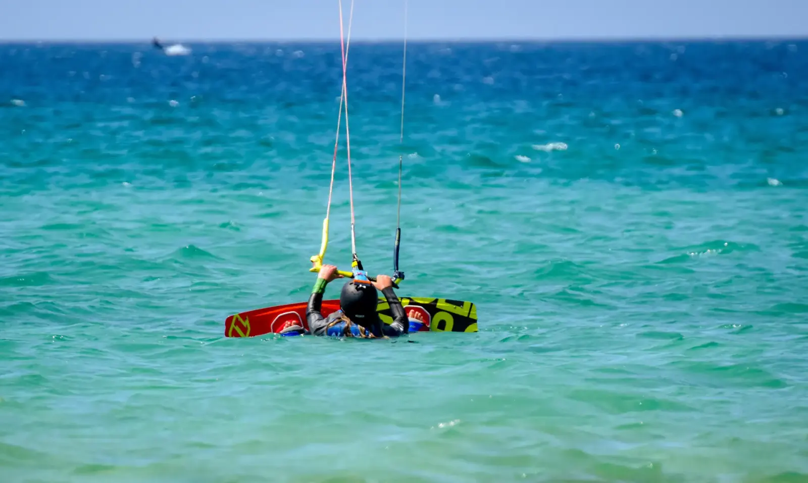 A student in turquoise water getting ready for a waterstart with the board on their feet