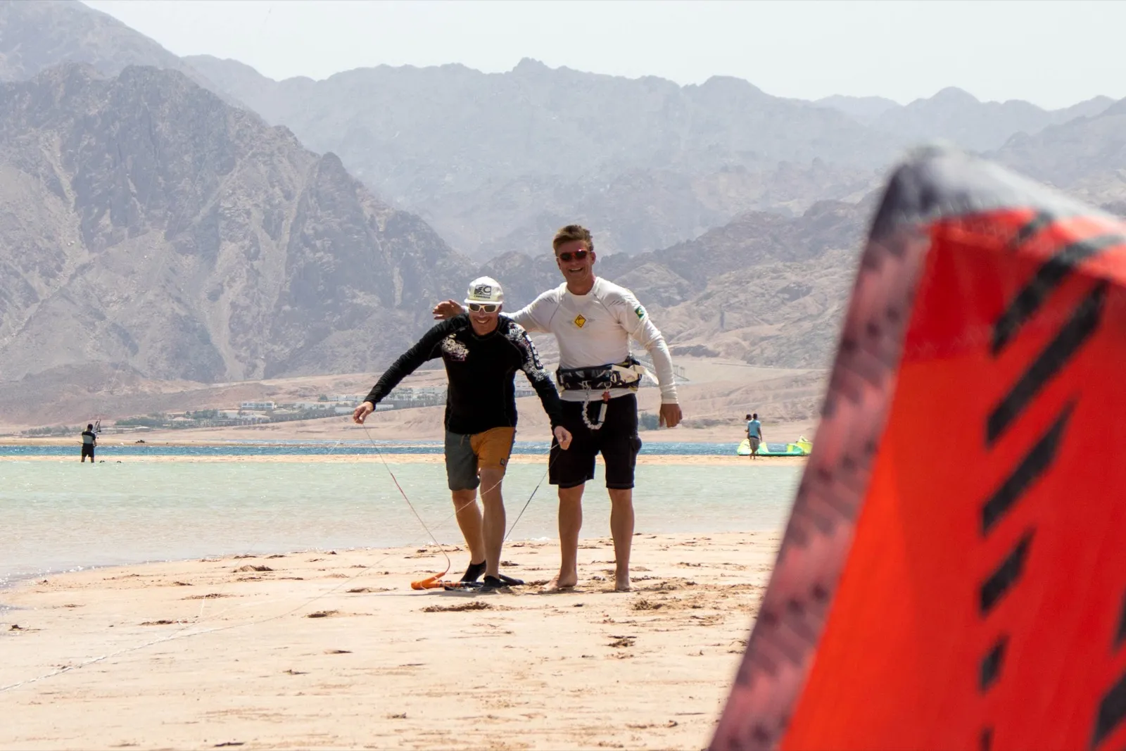 Two kitesurfers laughing together on the beach at Dahab Lagoon