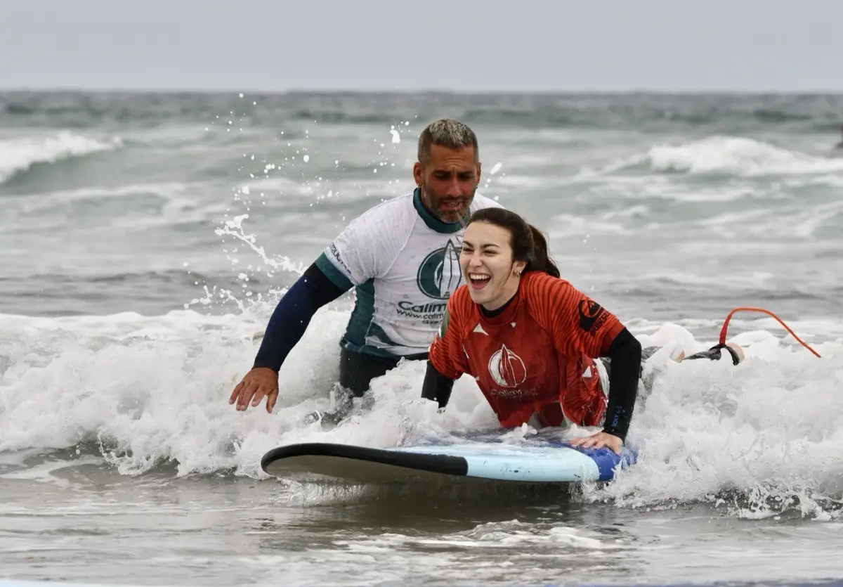 A Calima instructor pushing a laughing student on her board into a wave