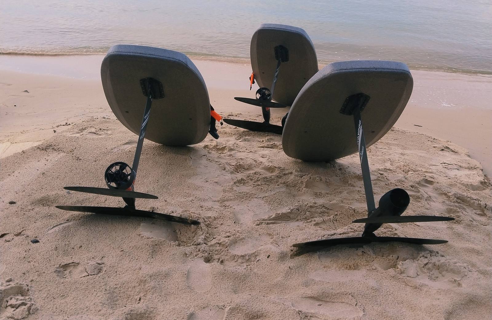 Three e-foil boards standing on the sand at the water's edge