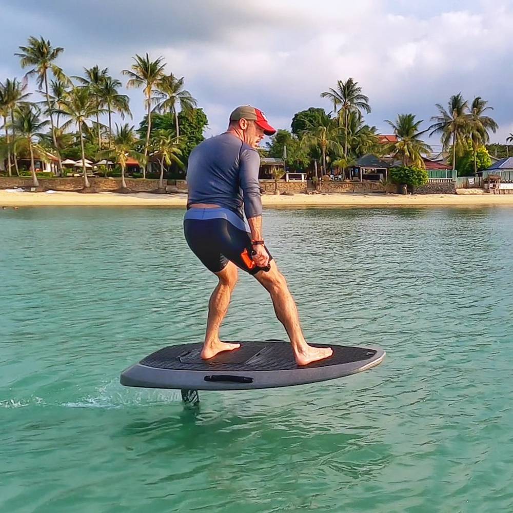 Rider carving on the e-foil in front of the palm-lined beach