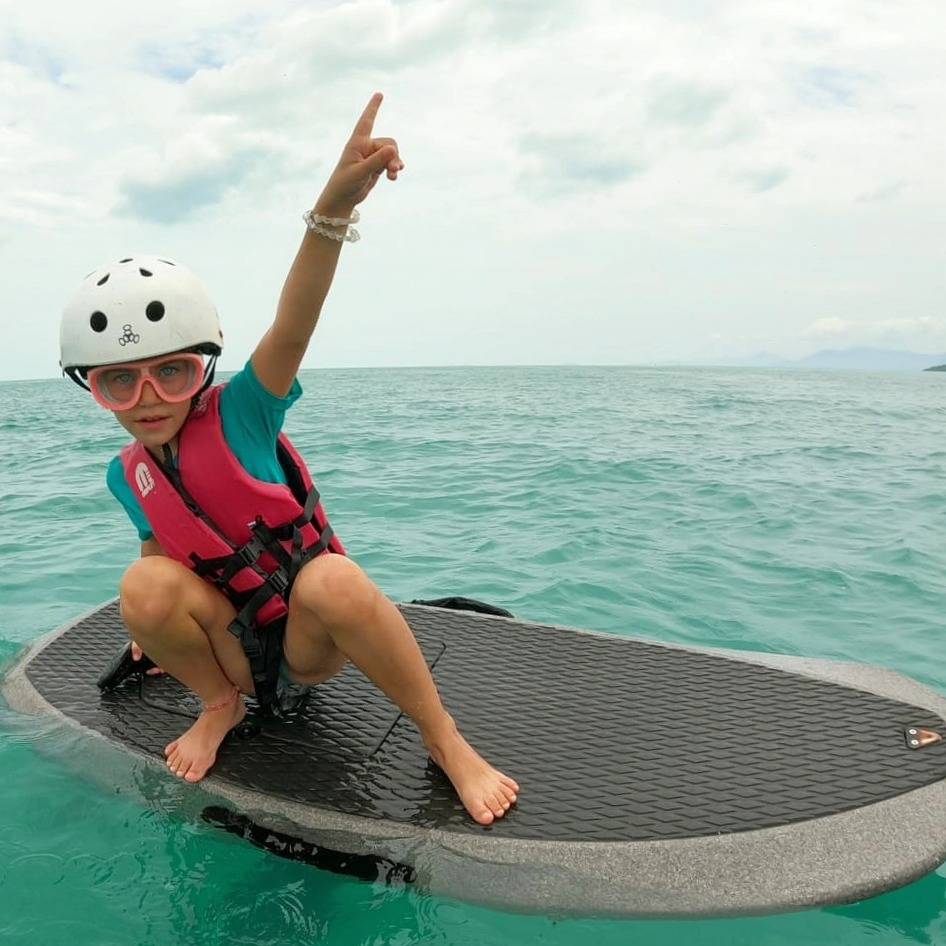 Kid in a helmet and life vest pointing up while riding the board