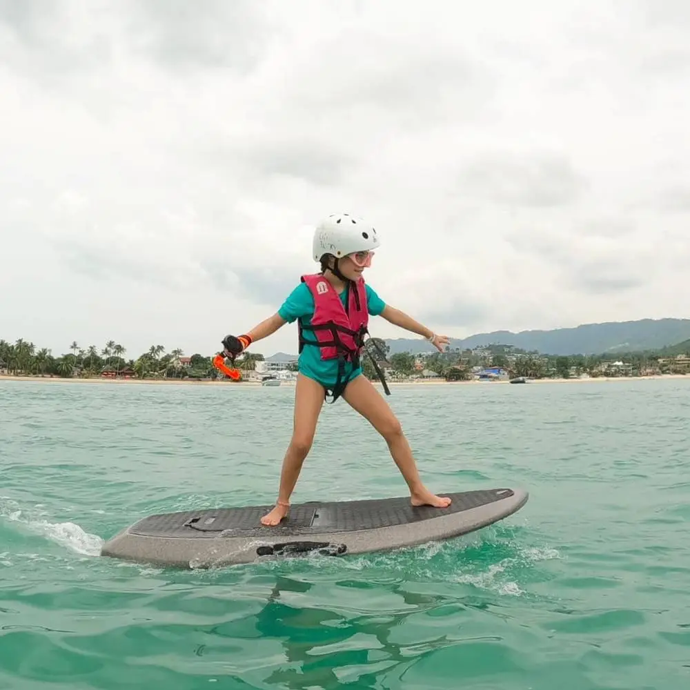 A kid in a helmet and life vest riding the e-foil standing up