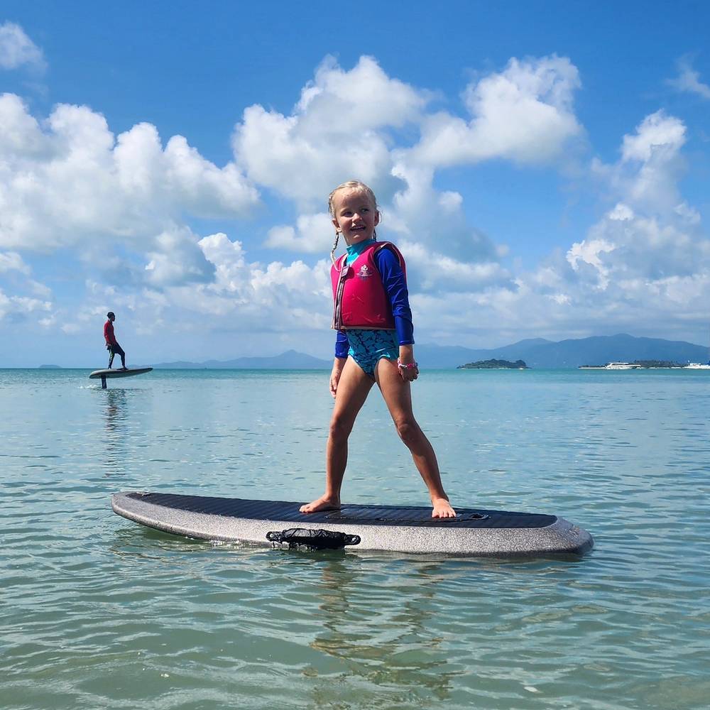Kid standing proudly on the board, riders in the bay behind