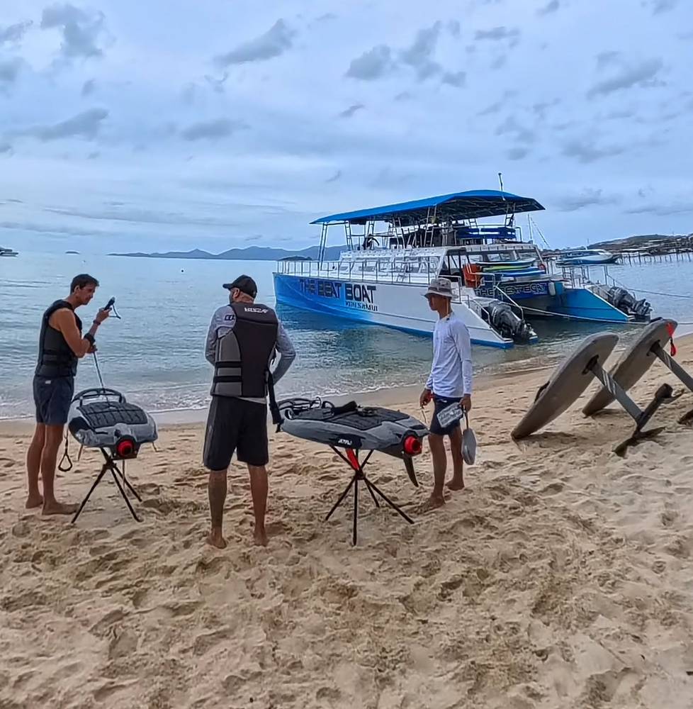 Team setting up the boards on the beach, a boat behind