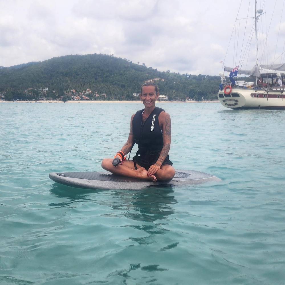 Guest sitting cross-legged on the board, a sailboat behind