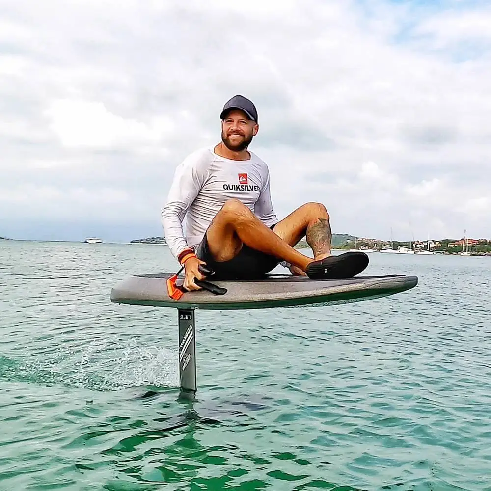 A guest sitting cross-legged on the e-foil while it flies above the water