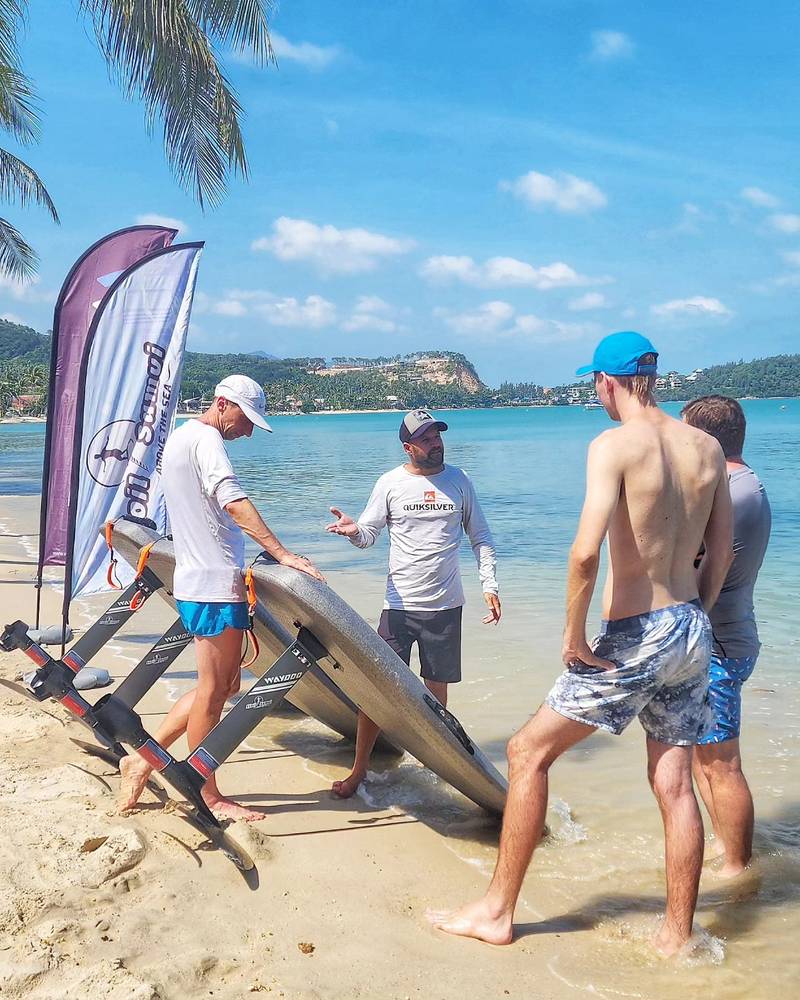 Team and guests carrying e-foil boards to the water past the Efoil Samui flag