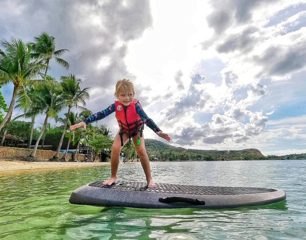 Young rider in a life vest standing on the board in the shallow bay