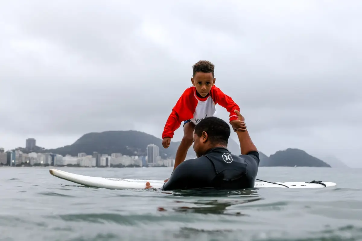 A school instructor in the water holding a young student up on a surfboard