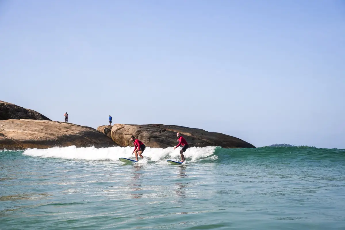 Two students in red school rash guards riding waves side by side
