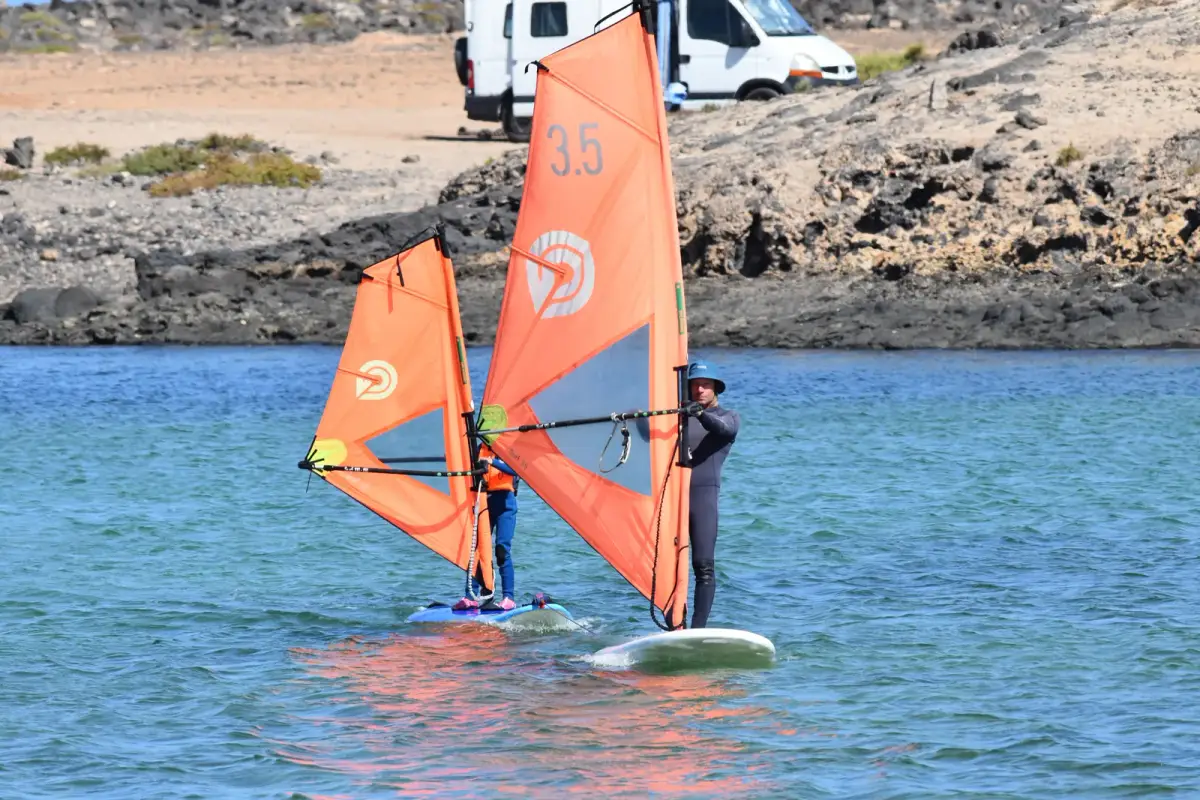 A Gecko instructor guiding a beginner on a windsurf board in the lagoon