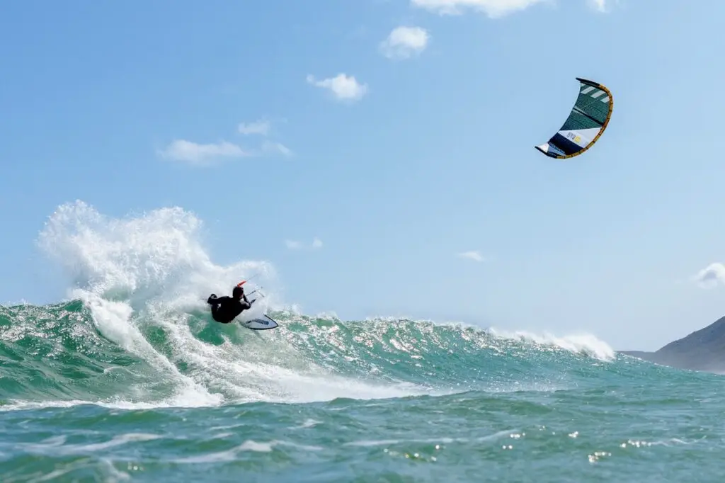 A rider on a kiteboard carving a wave under a blue sky in Cape Town