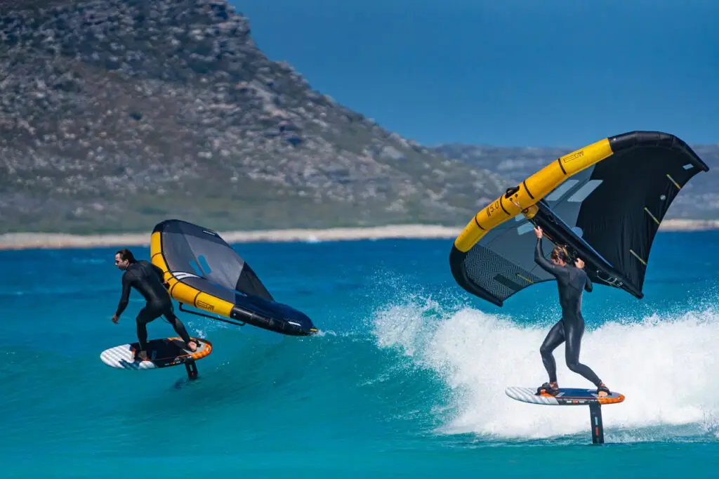 Two wing foilers riding a breaking wave in front of a mountain coast near Cape Town