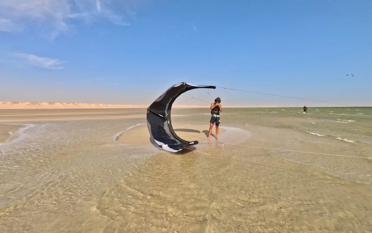 A kite resting on the shallow lagoon water with a person standing next to it