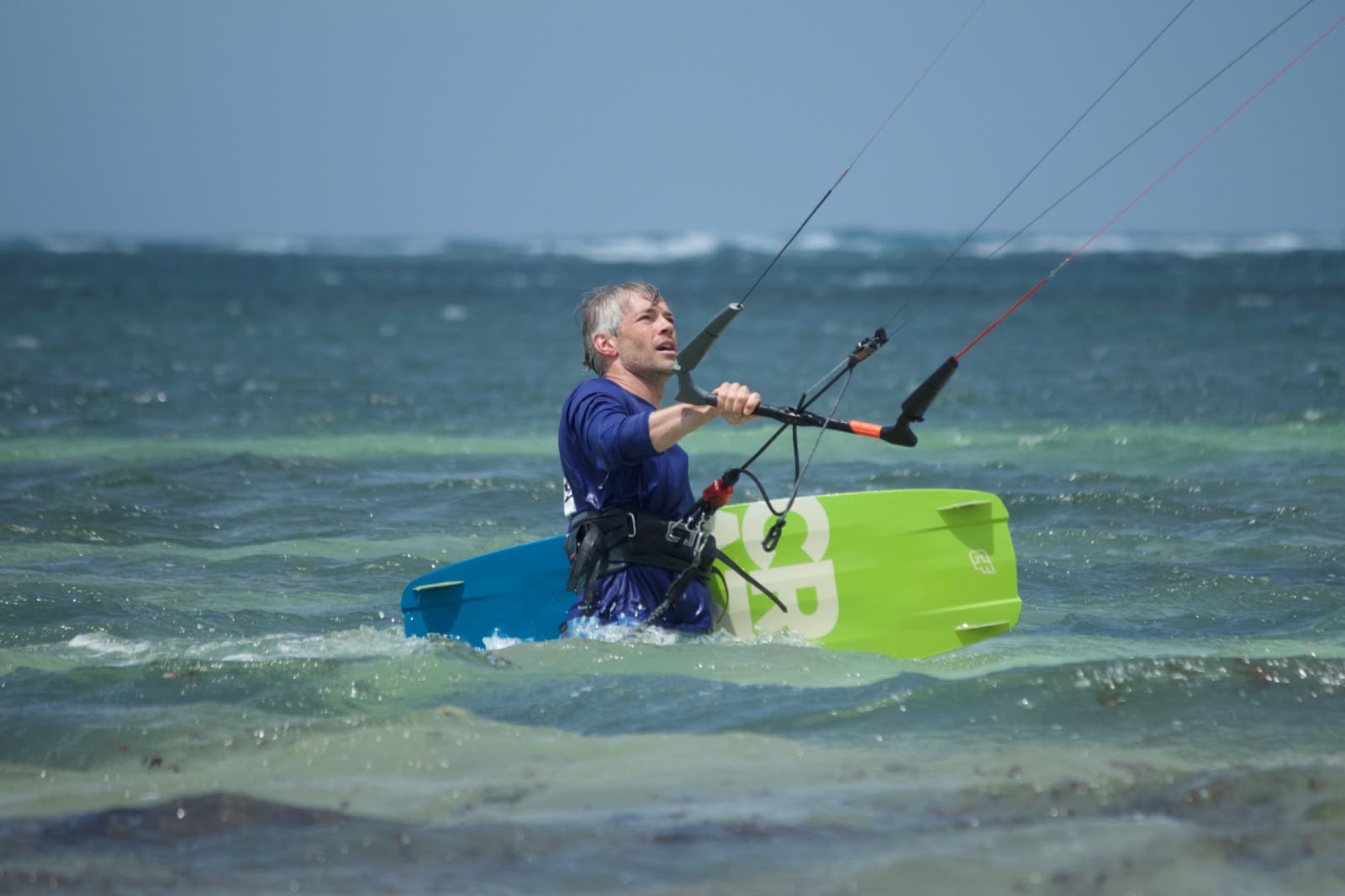 Kitesurfer in the water holding the control bar next to a blue and green board