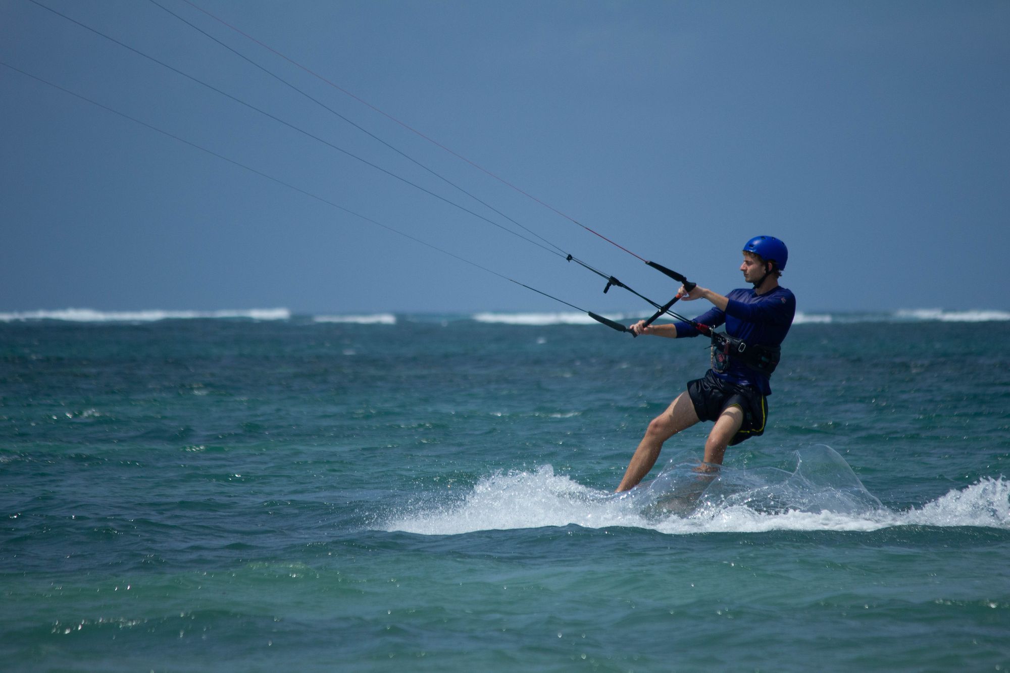 Kitesurfer in a blue helmet riding across the water, seen from the side