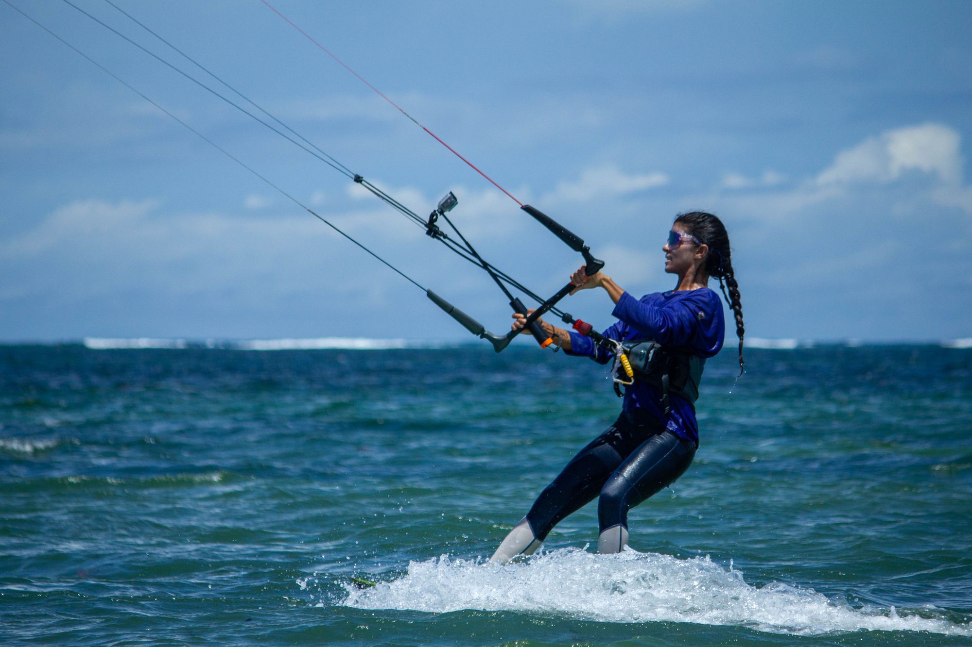 Kitesurfer with braids and sunglasses riding across the water