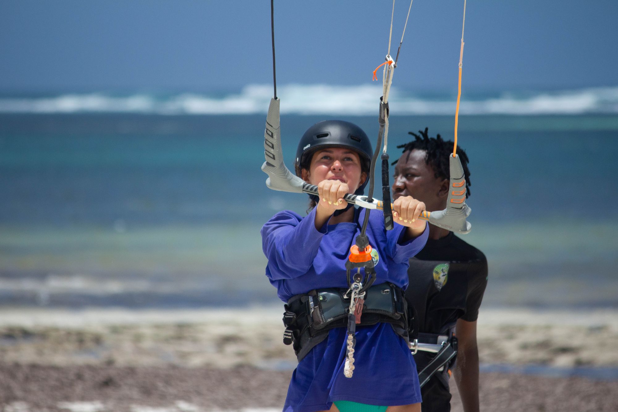 Student in a helmet holding the control bar, an instructor in a black shirt standing behind her