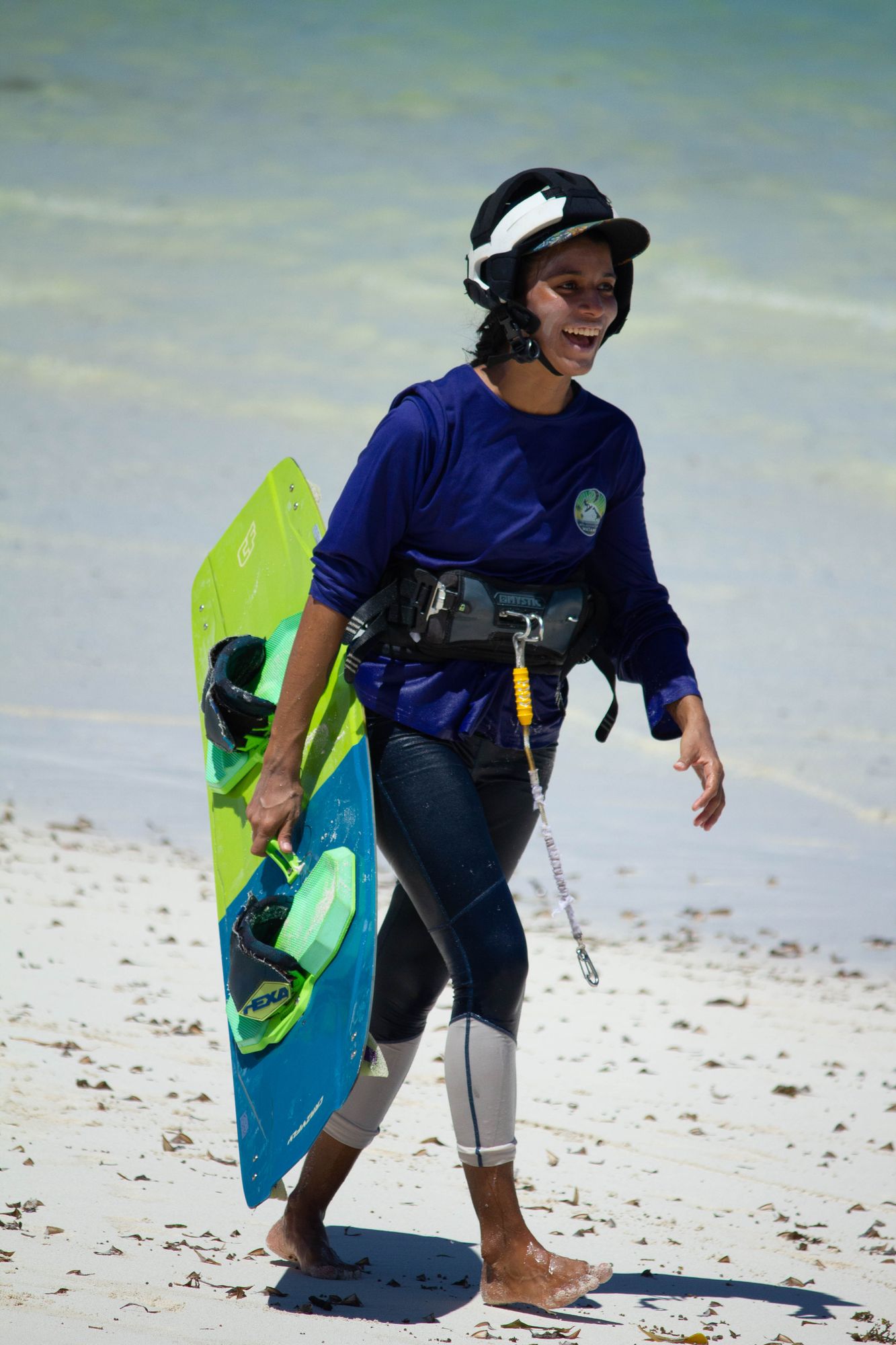 Smiling student in a helmet walking up the beach carrying a board