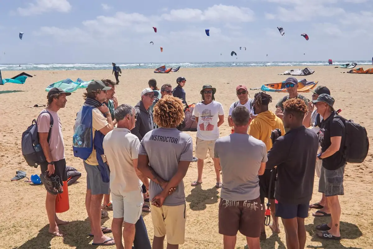 Group briefing on Kite Beach with kites in the sky behind