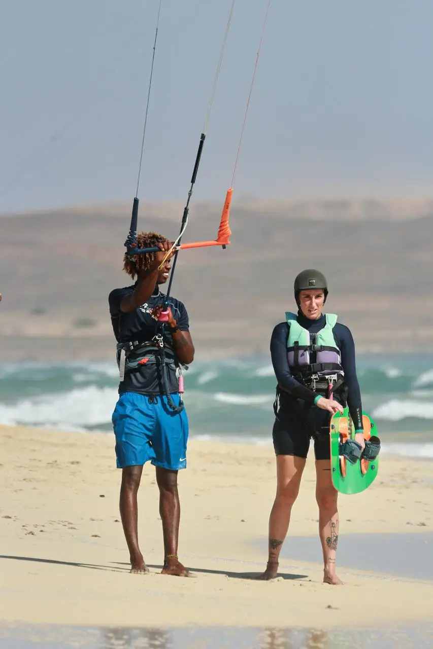 Instructor and a student in a helmet and impact vest at the water's edge, the student holding the control bar