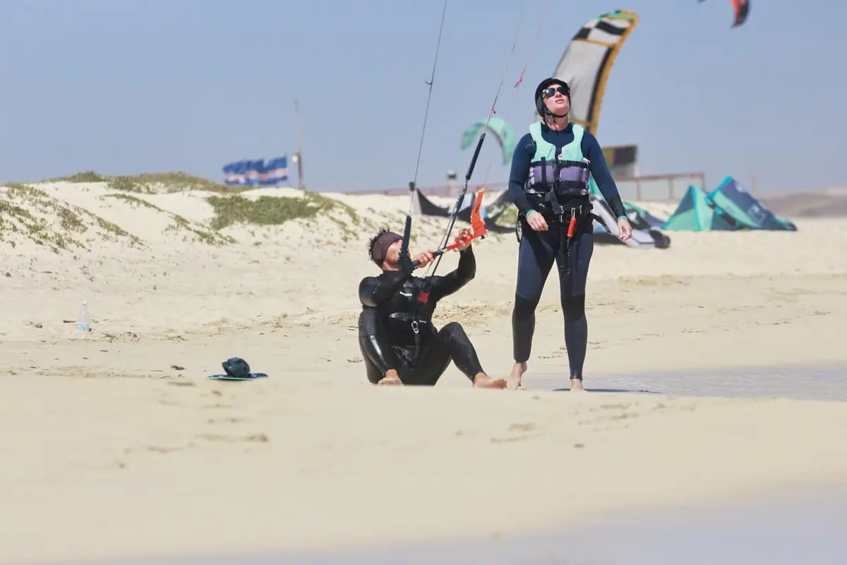 Instructor standing next to a student sitting in the sand with the kite in the air