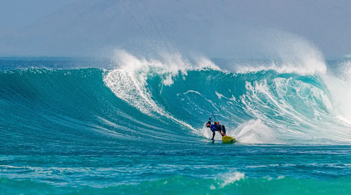 Kitesurfer on a yellow board carving a bottom turn under a big wave