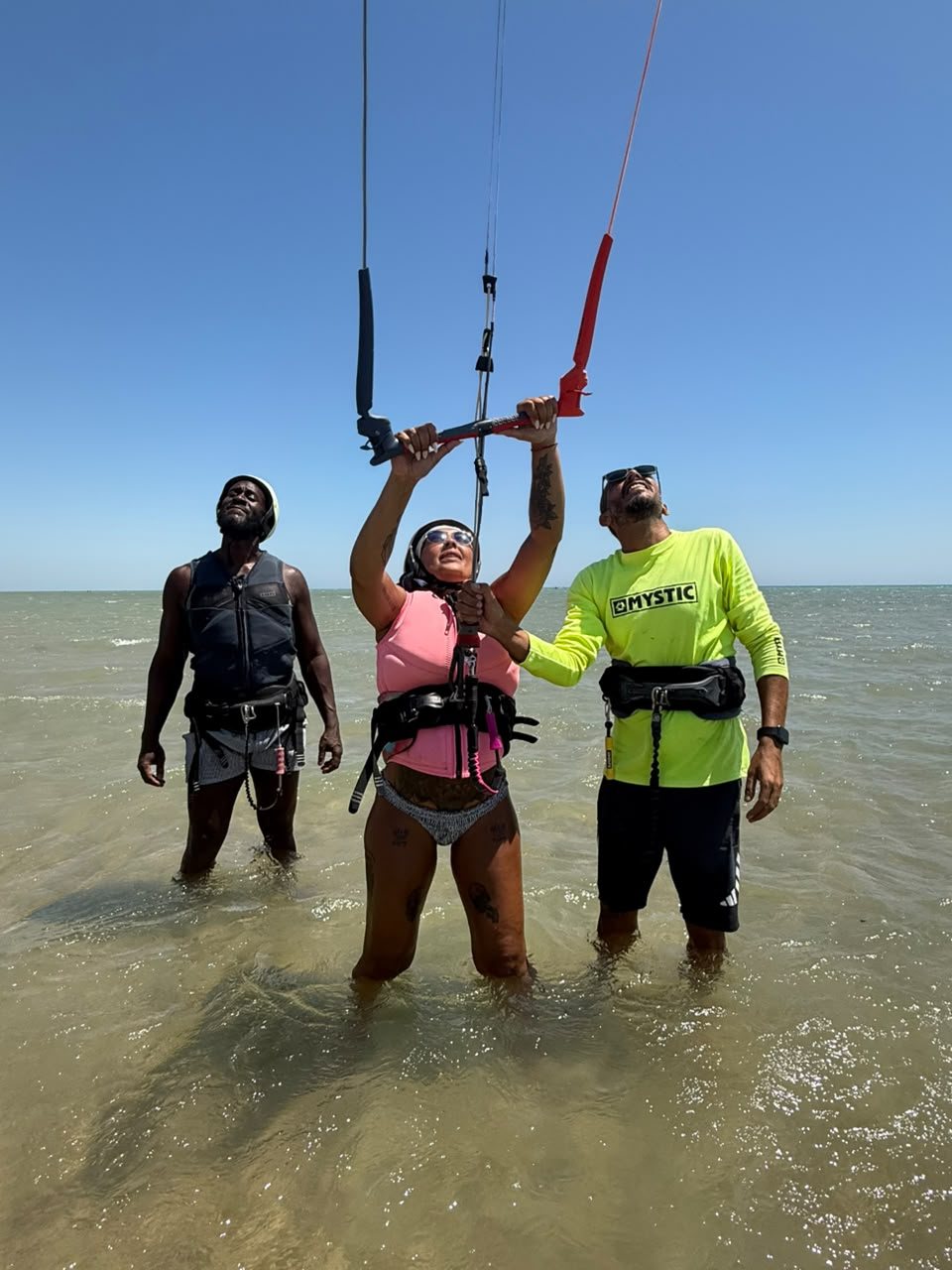 Instructor and two students holding a kite control bar in shallow water
