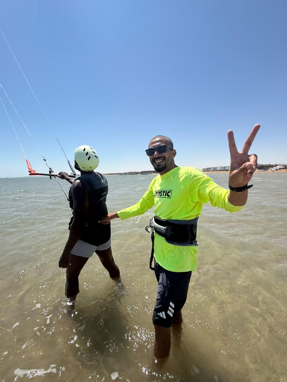 Instructor in a neon yellow shirt making a victory sign next to a student in shallow water