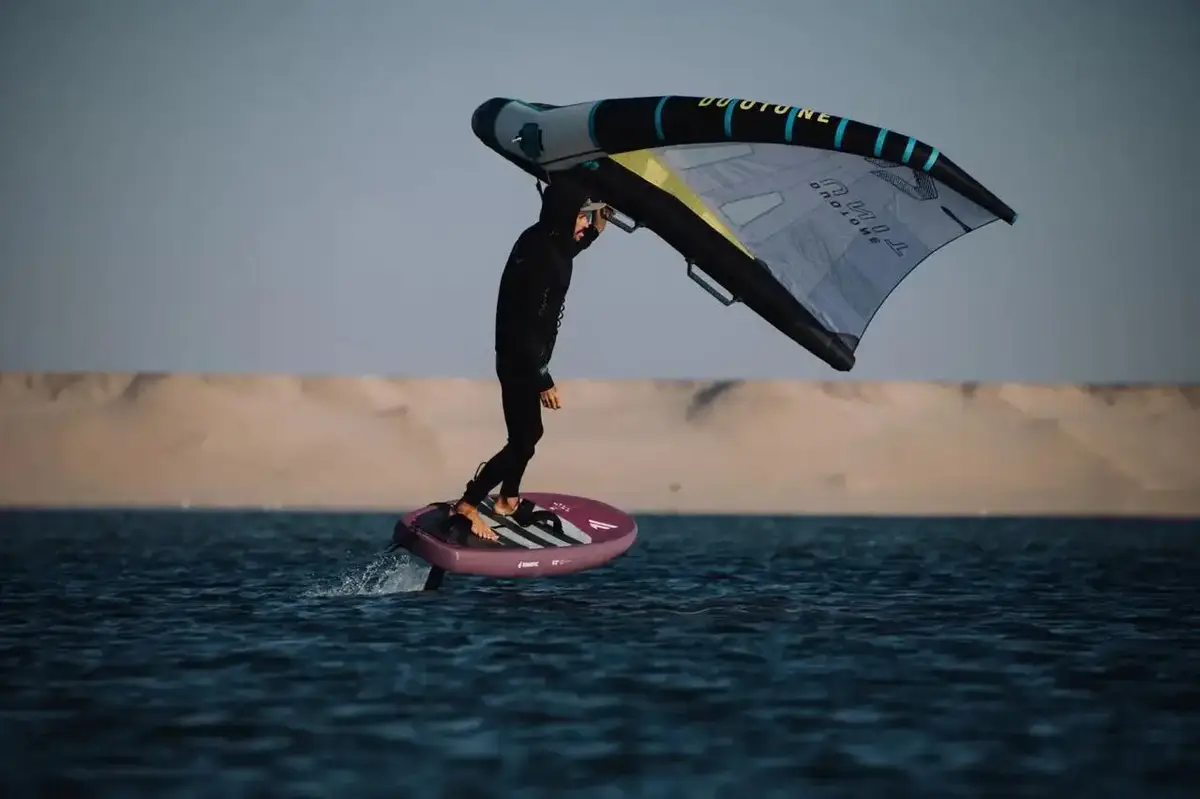 A wing foiler on a board in front of the dunes of the Dakhla lagoon