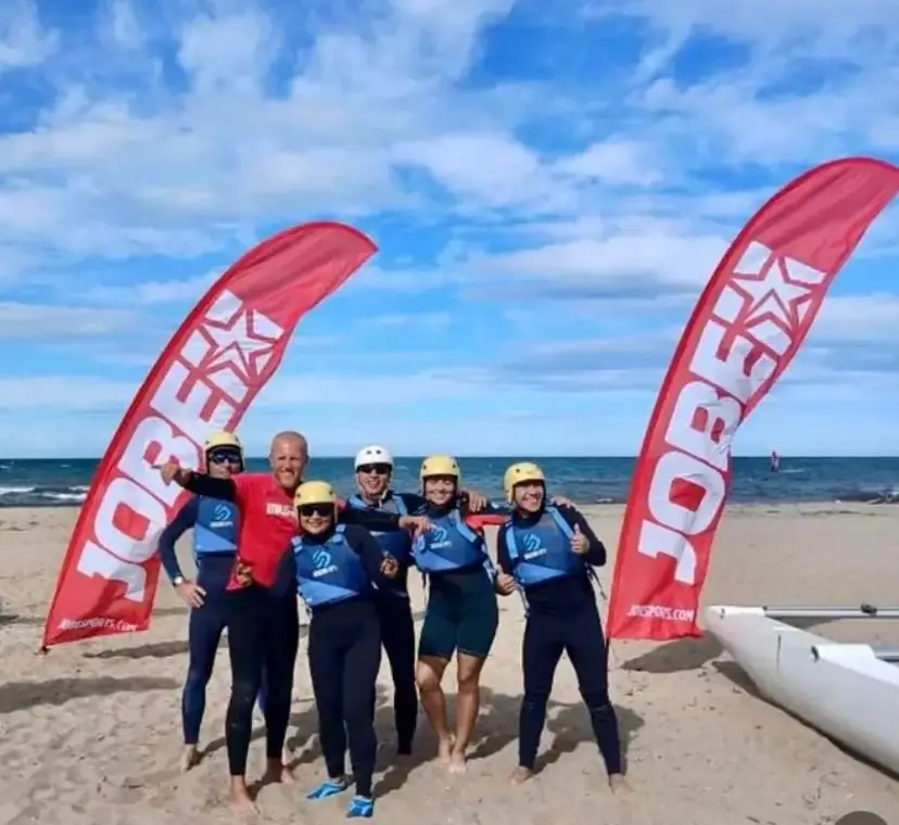 Group of students and instructors in blue vests and helmets posing on the beach between two red flags