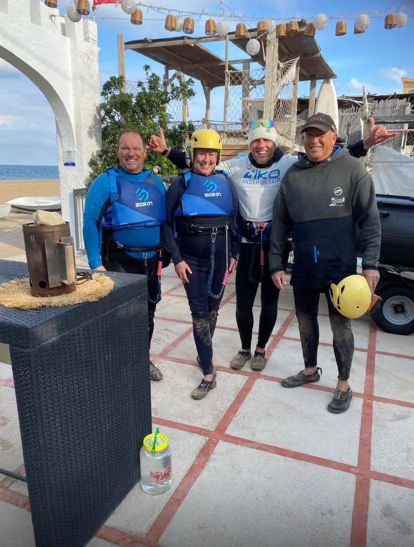 Four instructors in vests and wetsuits smiling together on a terrace next to a white building