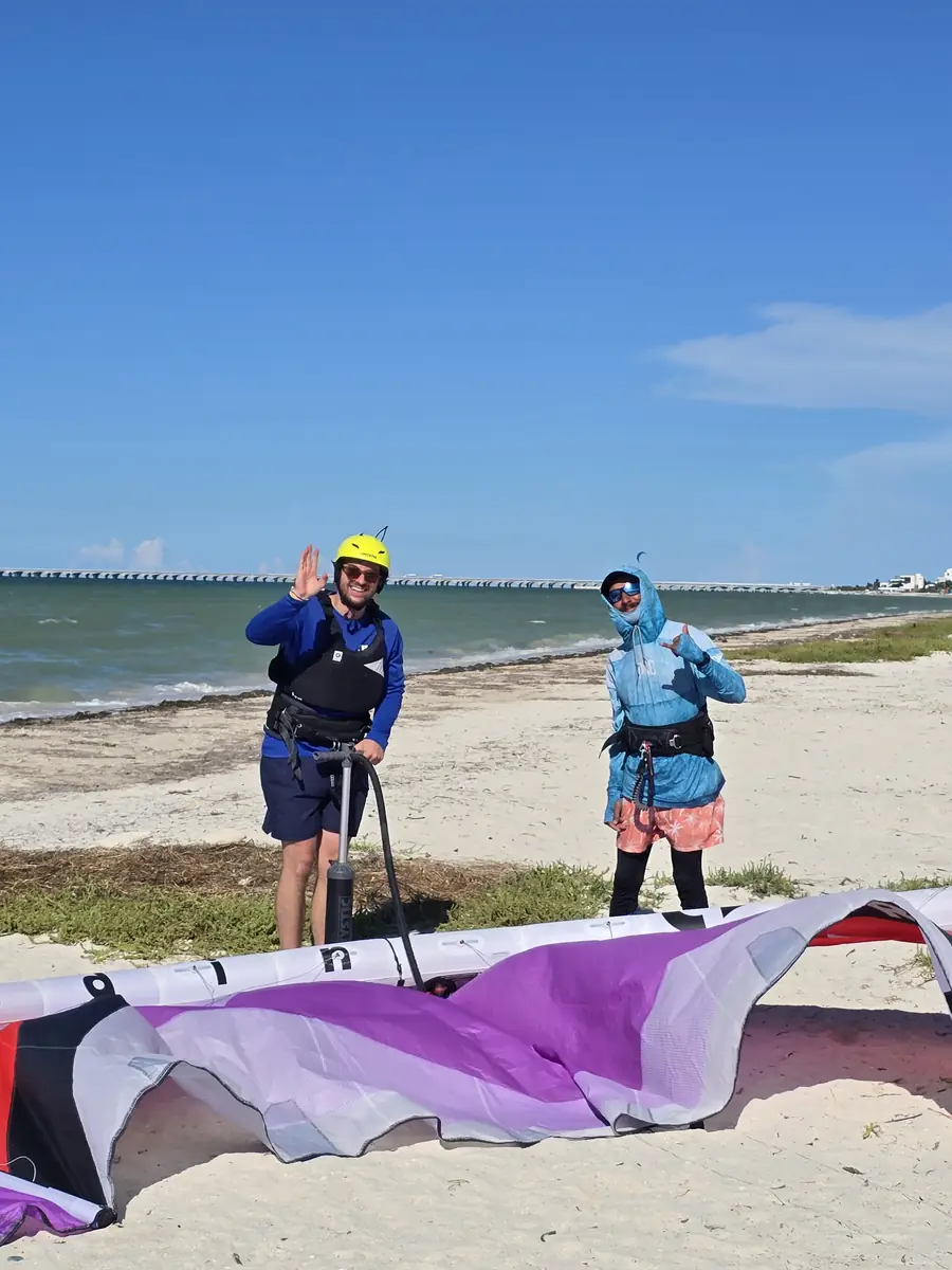 Instructor and student in a yellow helmet pumping up a purple kite on the beach, the sea and the Progreso pier behind