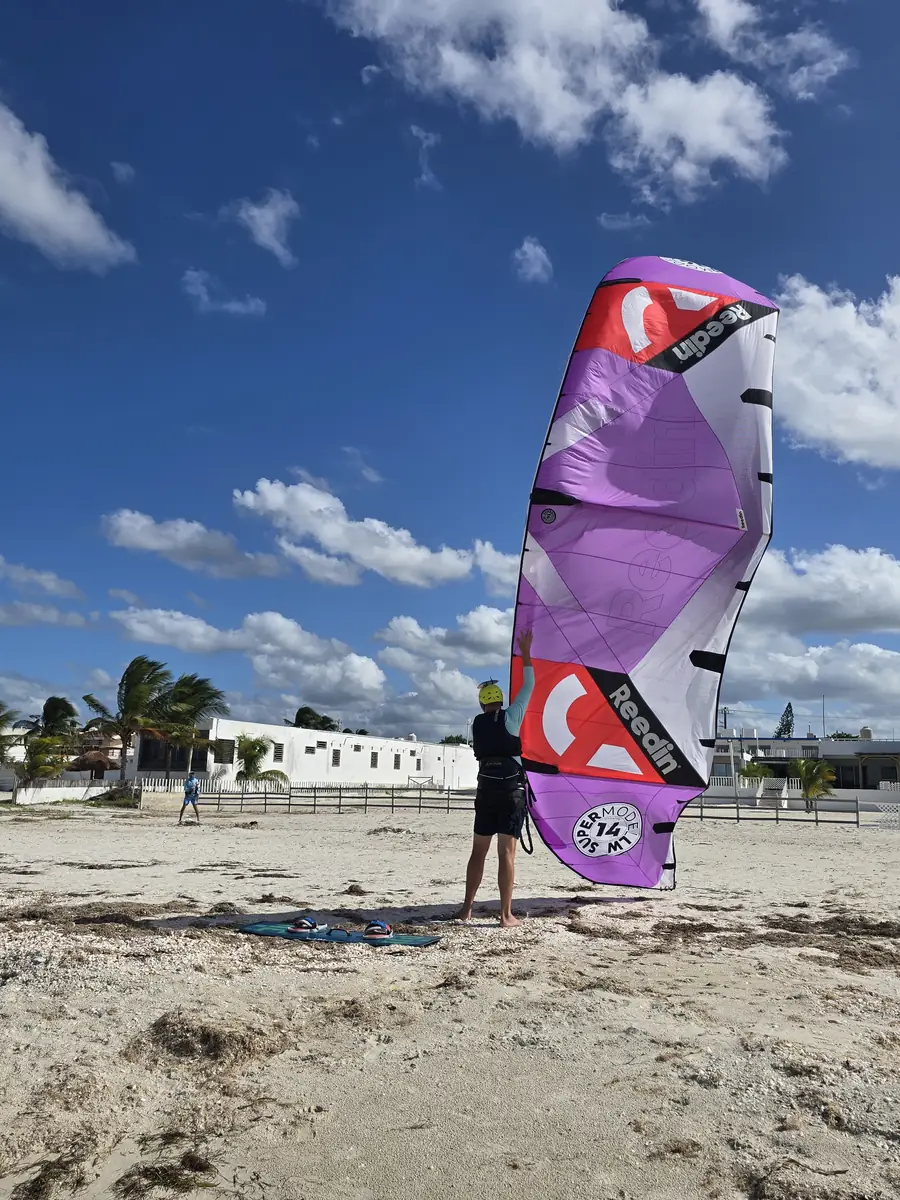 Student standing on the sand while a purple kite stands in the air for launching