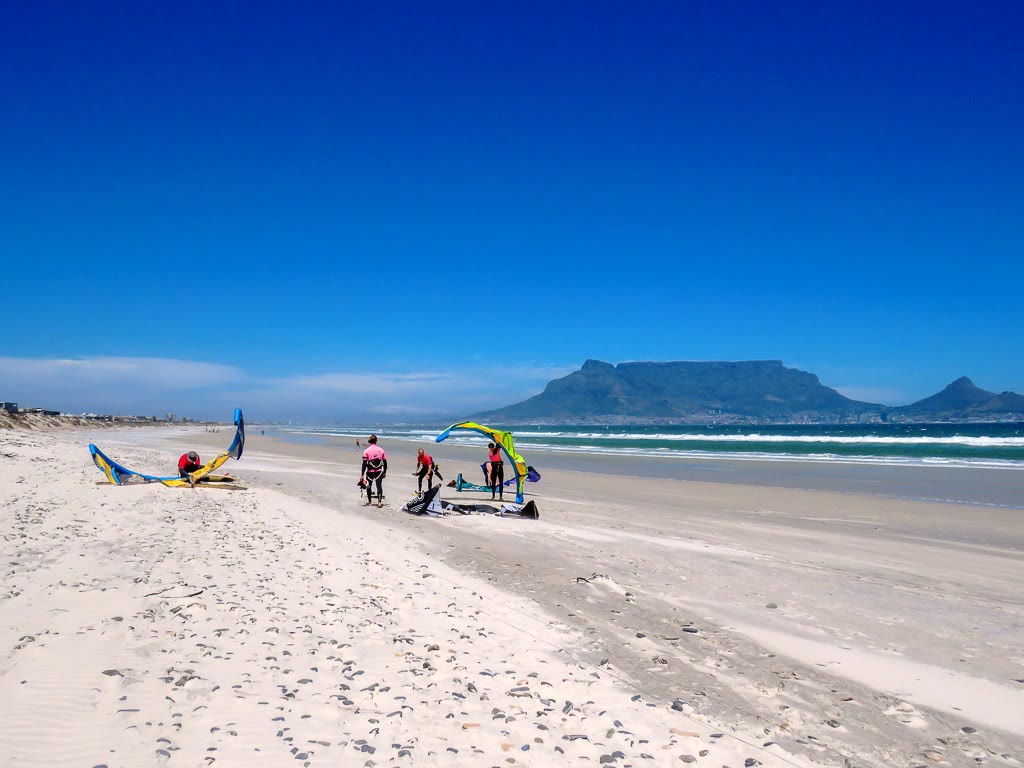 Long white beach with kites and riders and Table Mountain in the distance