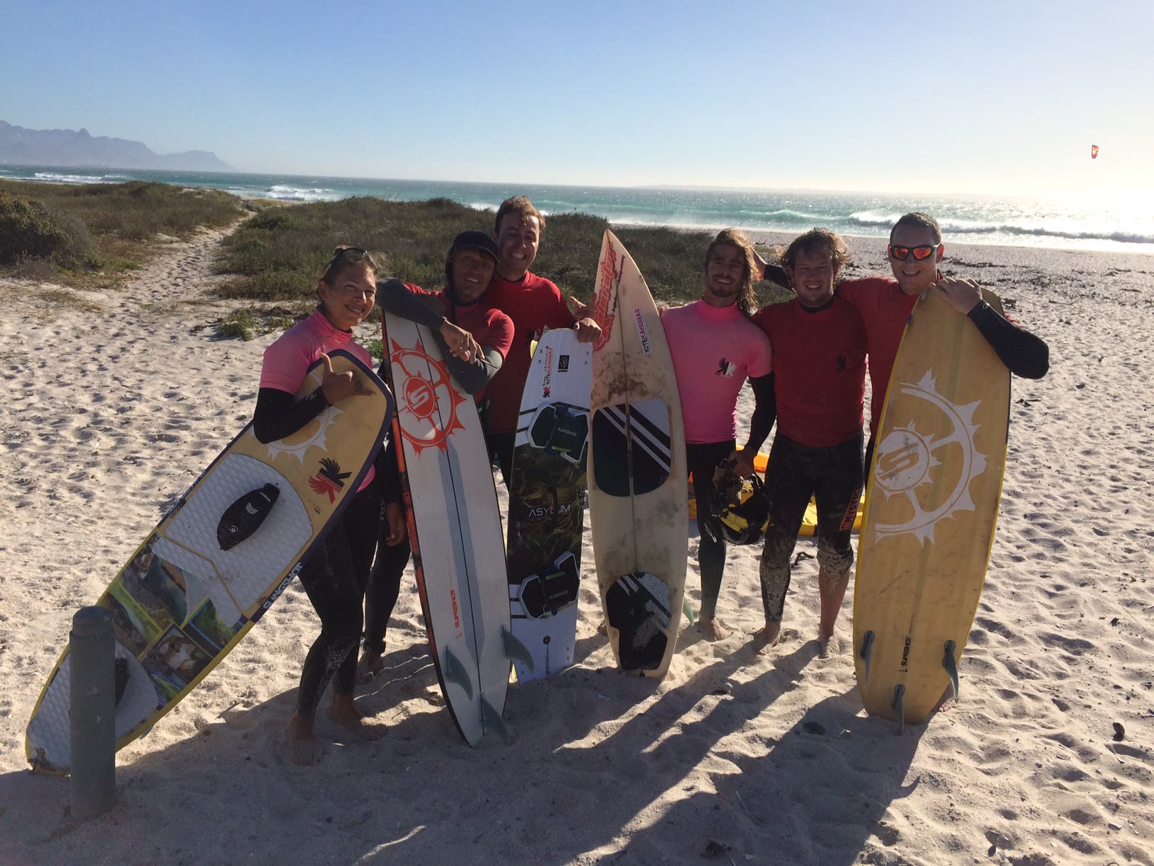 Group of smiling riders on a sandy path holding their boards