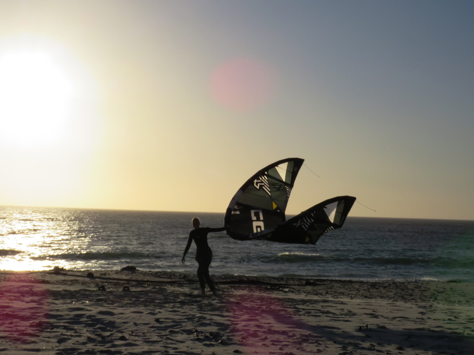 Rider launching a kite on the beach against the low sun