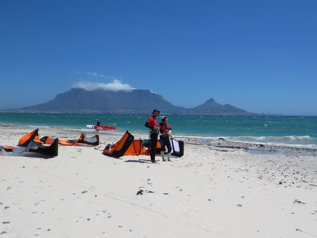 Kites laid out on a white beach with Table Mountain across the bay