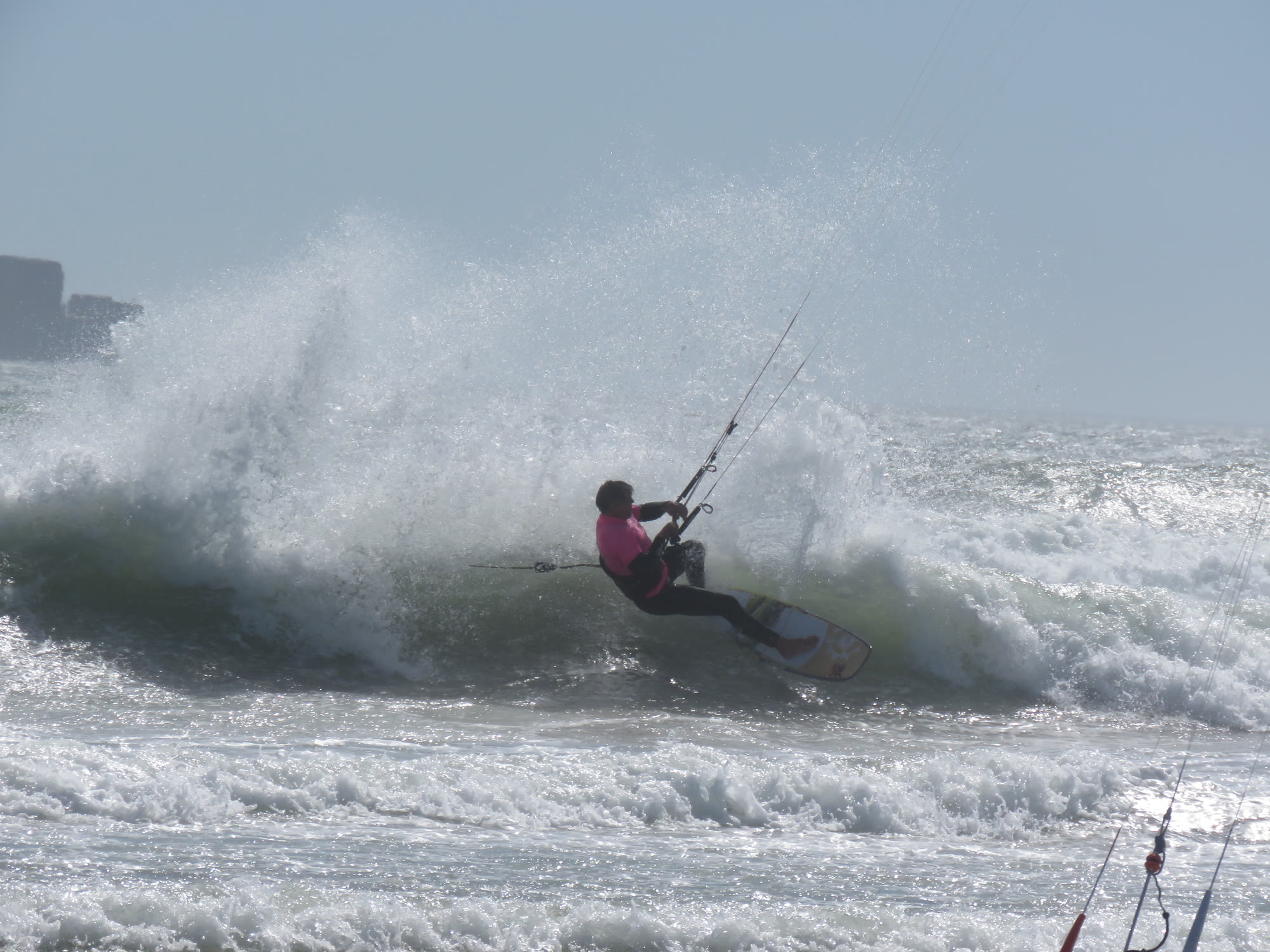 Kitesurfer carving through a breaking wave in a burst of spray