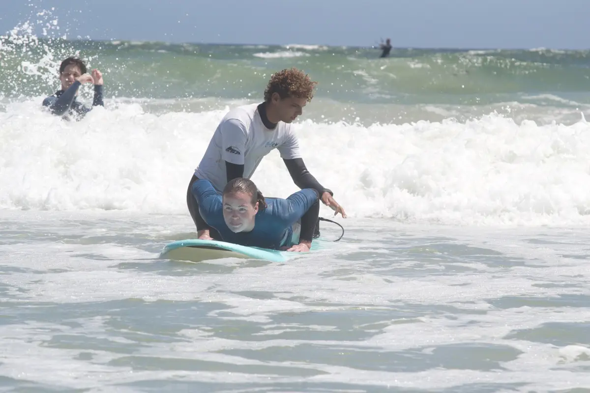 A Surf Life coach helping a student on a soft-top board in the whitewater