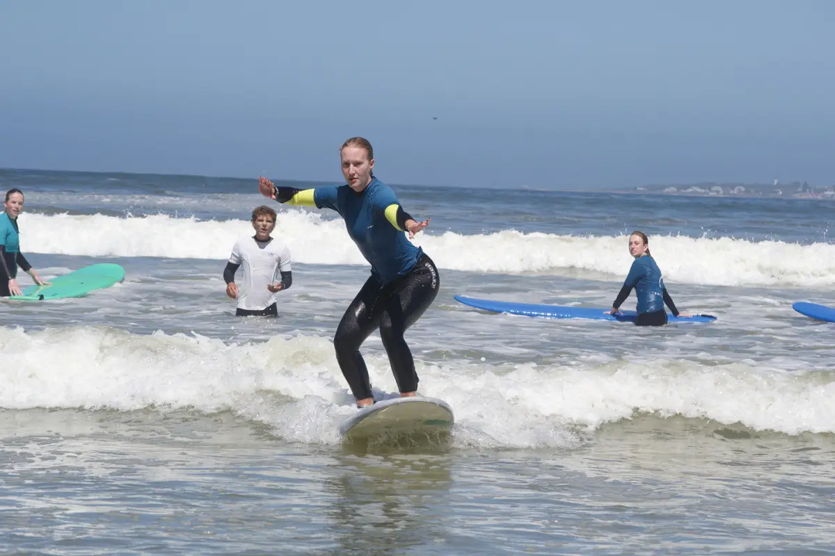 A student standing up on a board in the whitewater while coaches and other students watch
