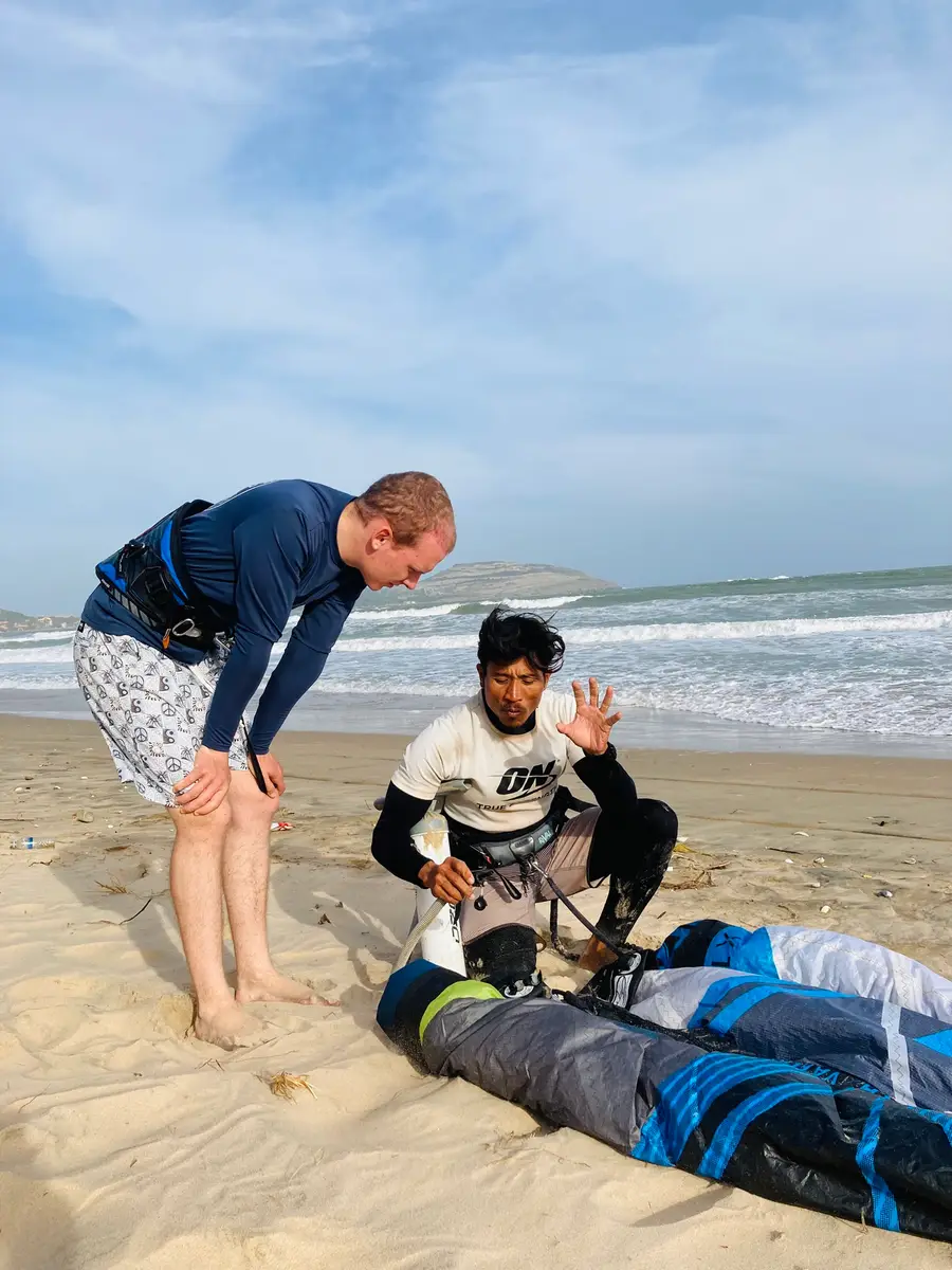 A UW Kite Surf instructor and a student on the beach in Mui Ne next to a kite bag during a kitesurf lesson