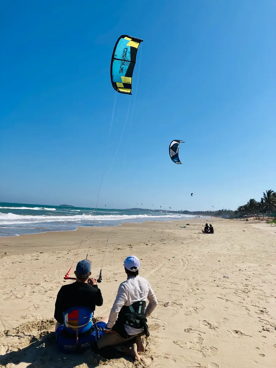 A student and an instructor on the sand in Mui Ne during a kite lesson, two kites flying over the bay